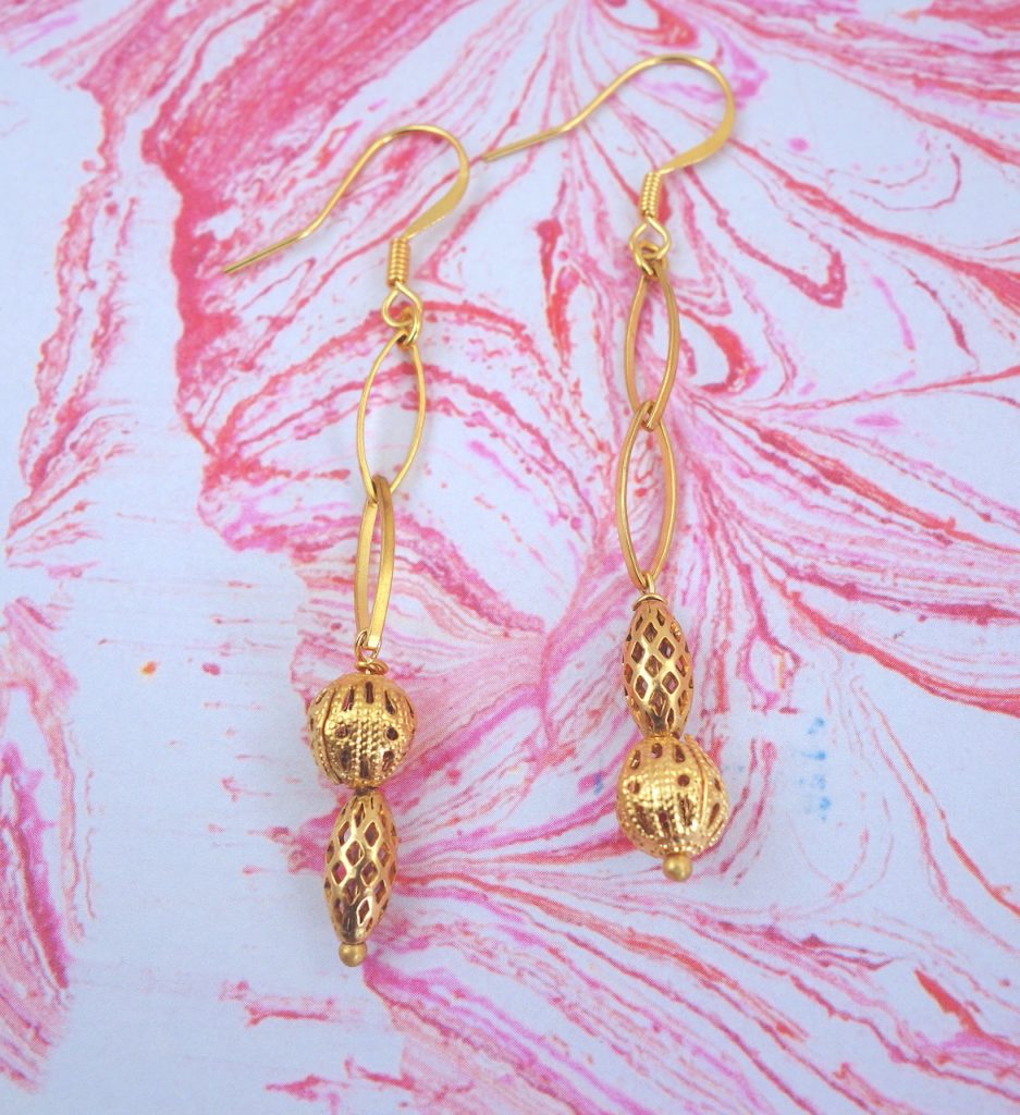 Boucles d'oreilles, attaches dormeuses, aux perles de laiton finement ouvragées, façon dentelle, disposées de manière asymétrique sur une chaîne graphique et aérienne, délicatesse arachnéenne.